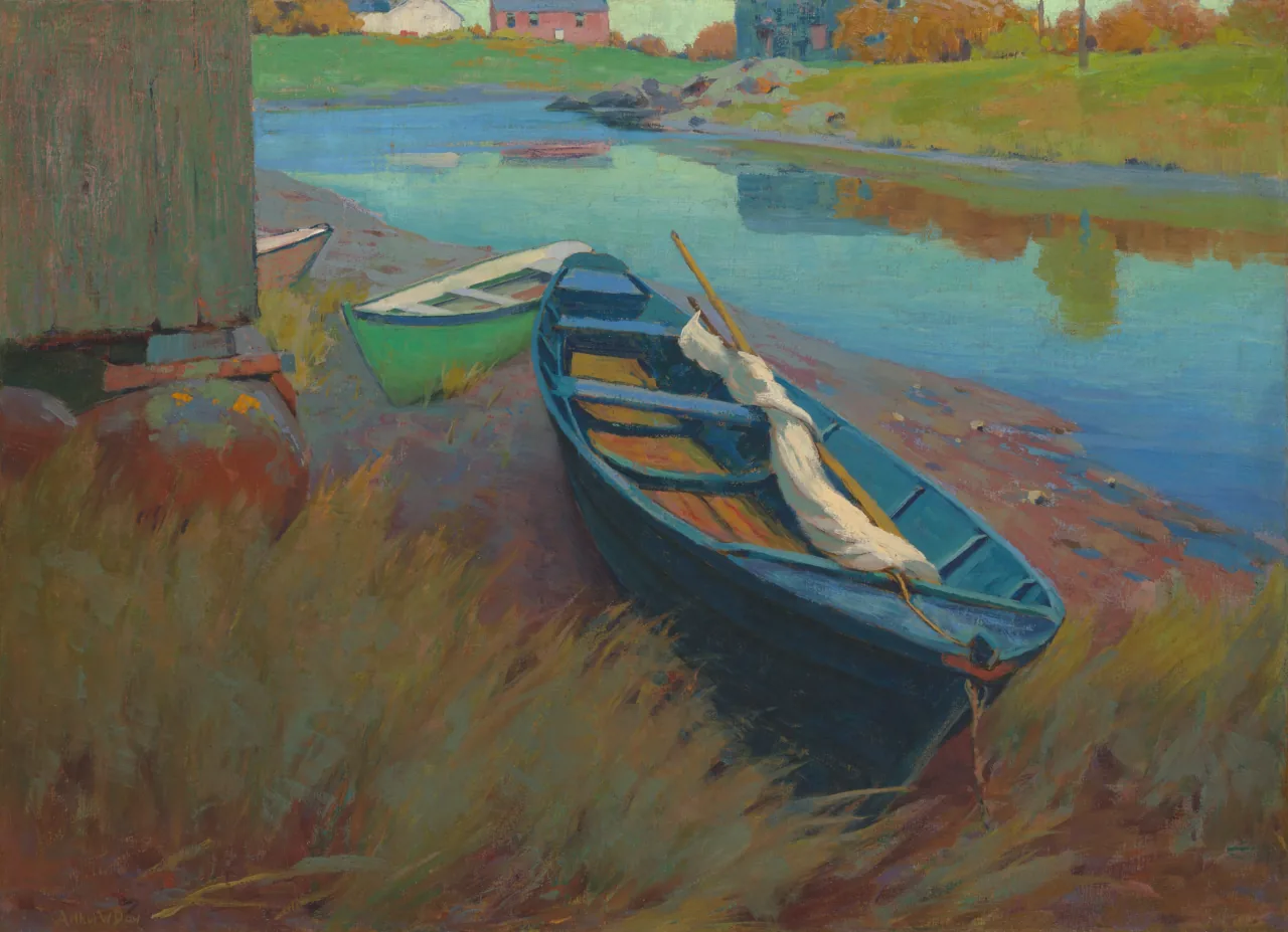 Three rowboats rest beside a cropped dark building at the edge of a blue-green harbor, with low houses and autumn trees across the water.